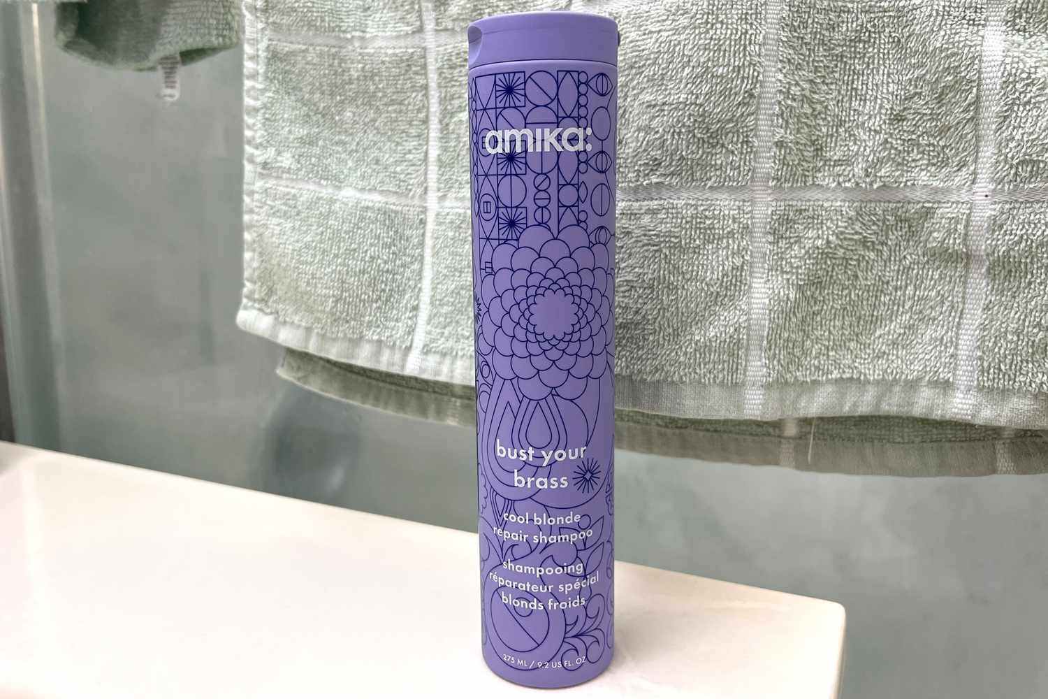A bottle of Amika Bust Your Brass Cool Blonde Repair Shampoo on a counter 