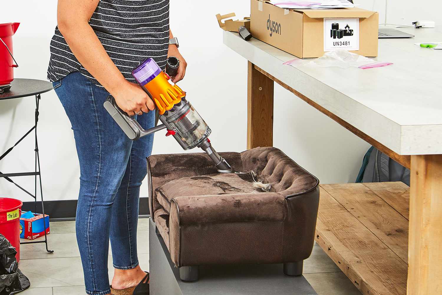 A person using a Dyson V12 Detect Slim to clean fur from a dog bed