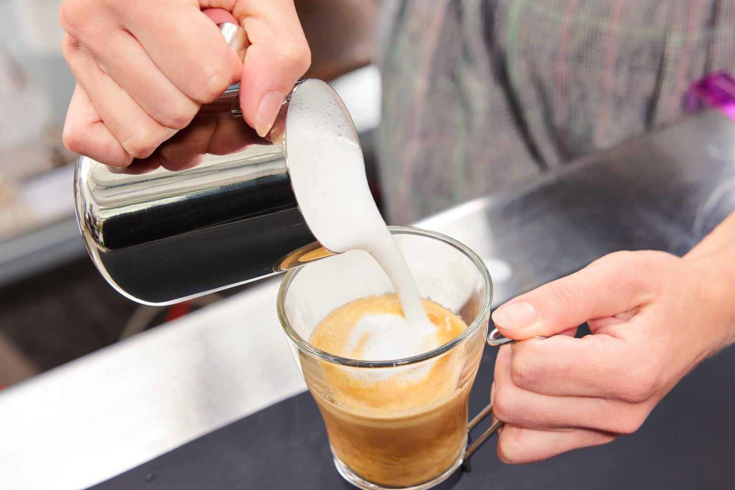 A person pours frothed milk into a cup of espresso.