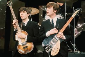 Paul McCartney and John Lennon hold their guitars while on the set of The Ed Sullivan Show 