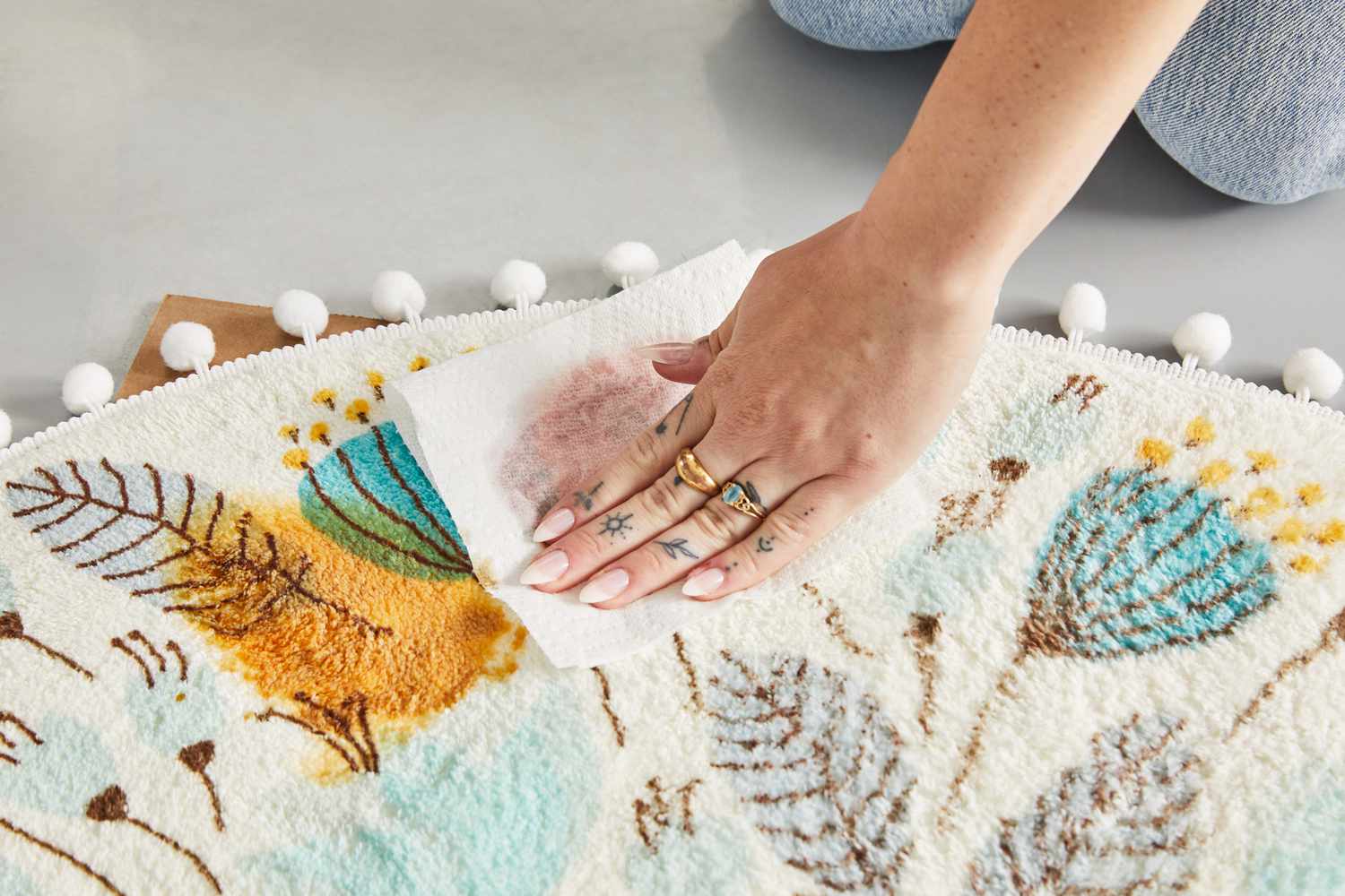 A person cleaning stains on the side of the Uphome Pom Pom Round Floral Rug with a paper towel