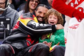 Rapper Drake embraces his son Adonis as the Raptor mascot brings over candy for him during the first half of the NBA game between the Toronto Raptors and the LA Clippers at Scotiabank Arena on December 27, 2022