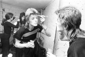 David Bowie Backstage at Lewisham, London, making up for a Ziggy Stardust concert with members of the band visible, reflected in the mirror. 