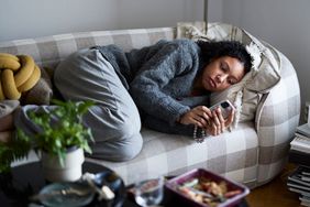 Pensive young woman lying on sofa and using phone