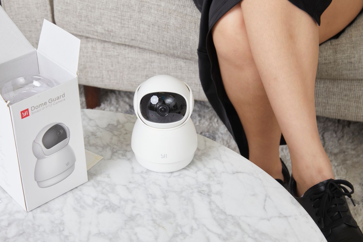 Person sitting on a couch next to the YI Technologies Dome Pet Camera and its box on a table