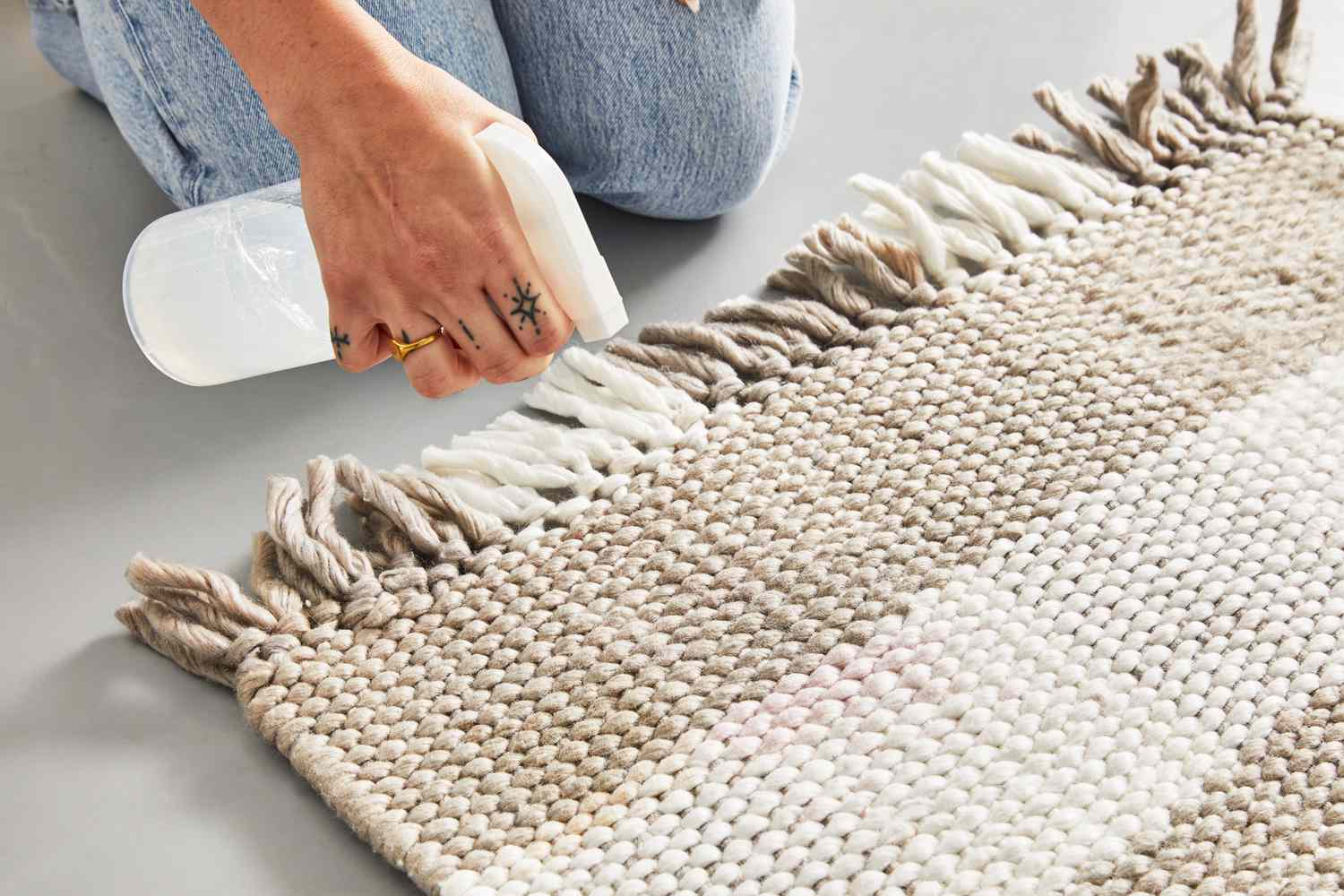 A person spraying a cleaning solution on the Rugs.com Washable Eco Plaid Indoor/Outdoor Rug