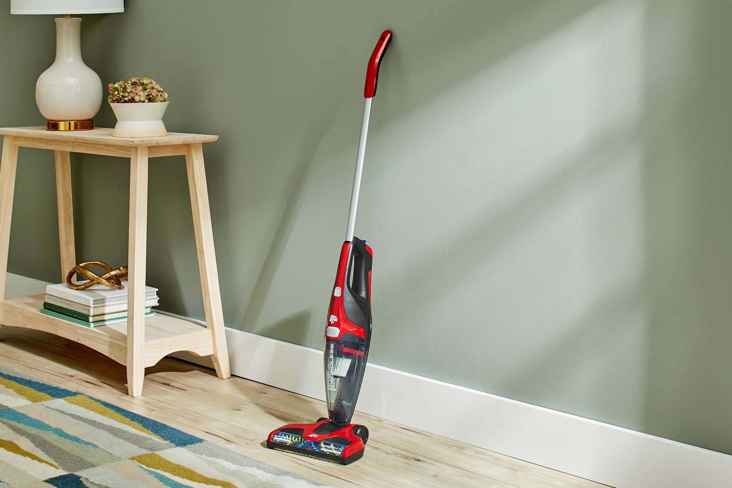 DirtDevil Versa Cordless 3-in-1 Stick Vacuum displayed in room next to carpet and stand with lamp