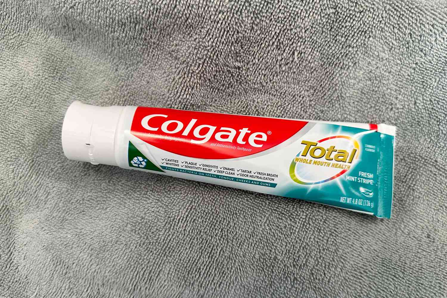 A tube of Colgate Total Fresh Mint Stripe Gel Toothpaste on a carpet