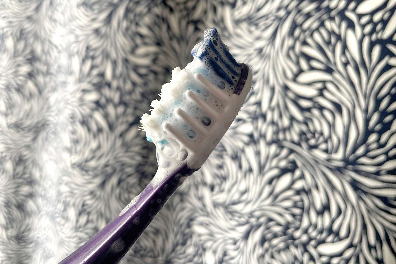 Sensodyne Extra Whitening Toothpaste lathered on a toothbrush in front of a shower curtain