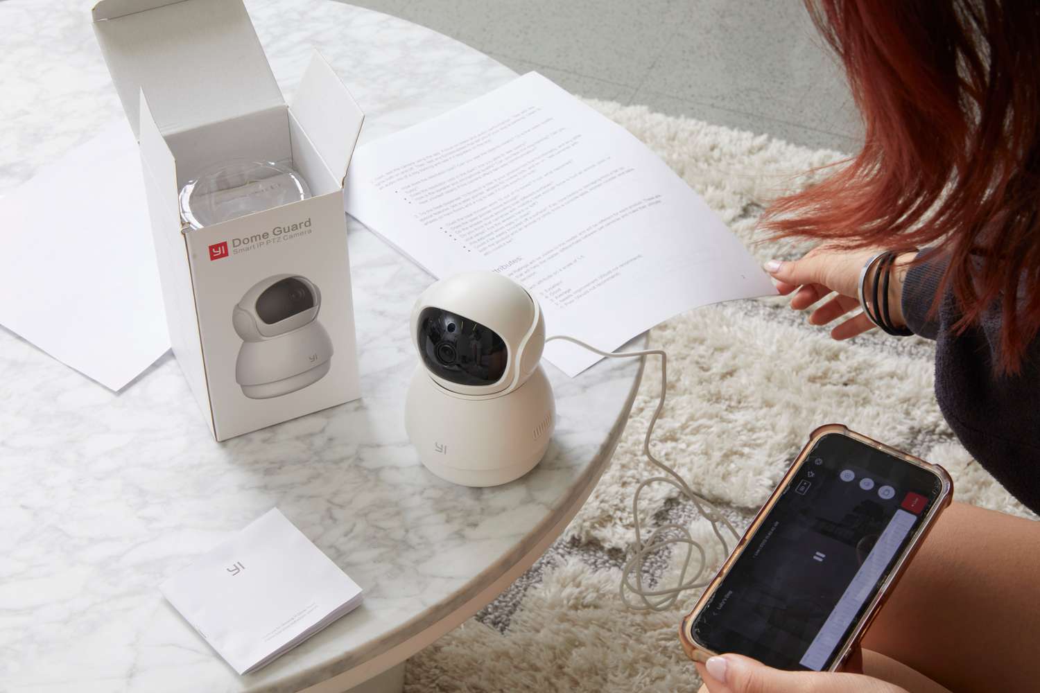 Person holding their phone with the YI Technologies Dome Pet Camera app displayed while looking at the instructions manual