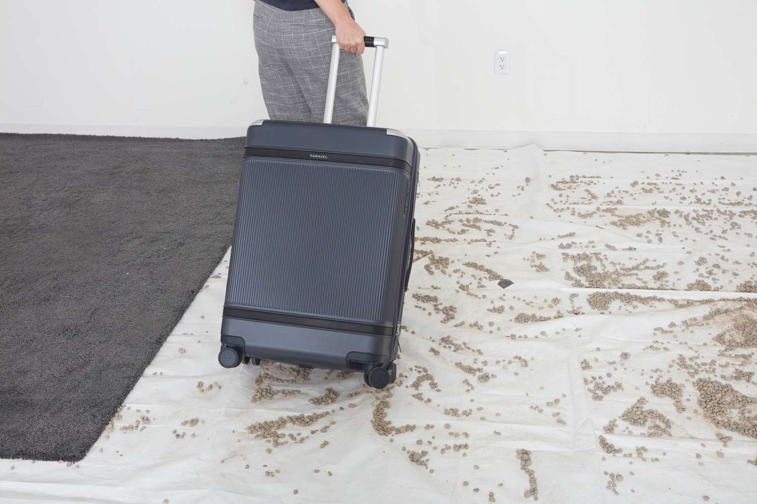 A person pulling the Paravel Aviator Grand Checked Luggage on a tarp with gravel