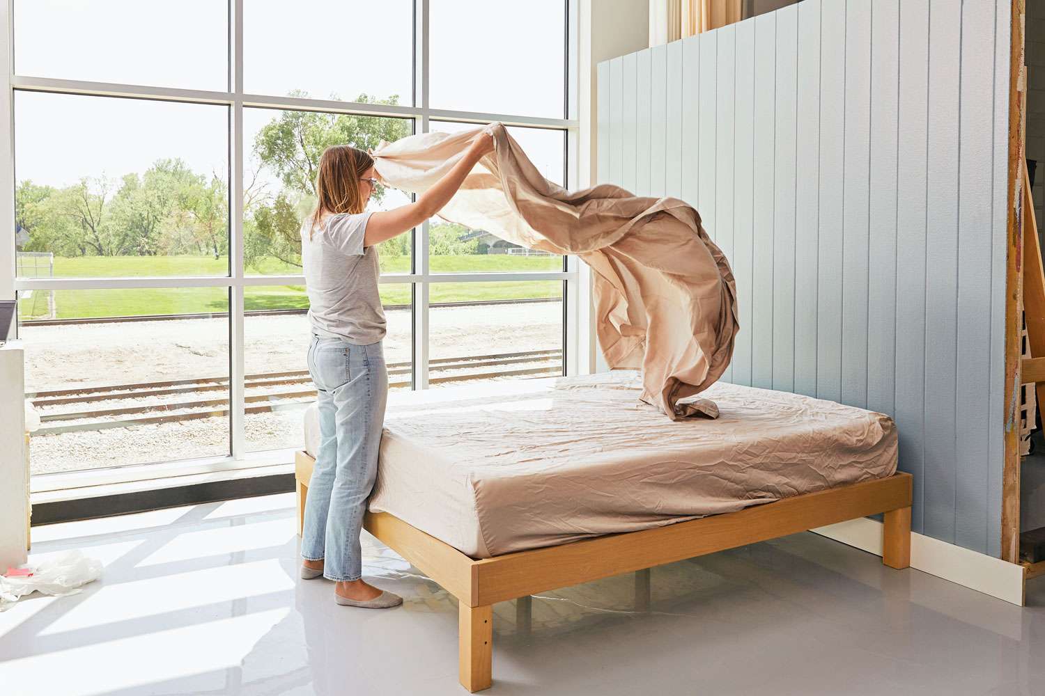 A woman holding a Cozy Earth Bamboo Sheet Set top sheet over the mattress