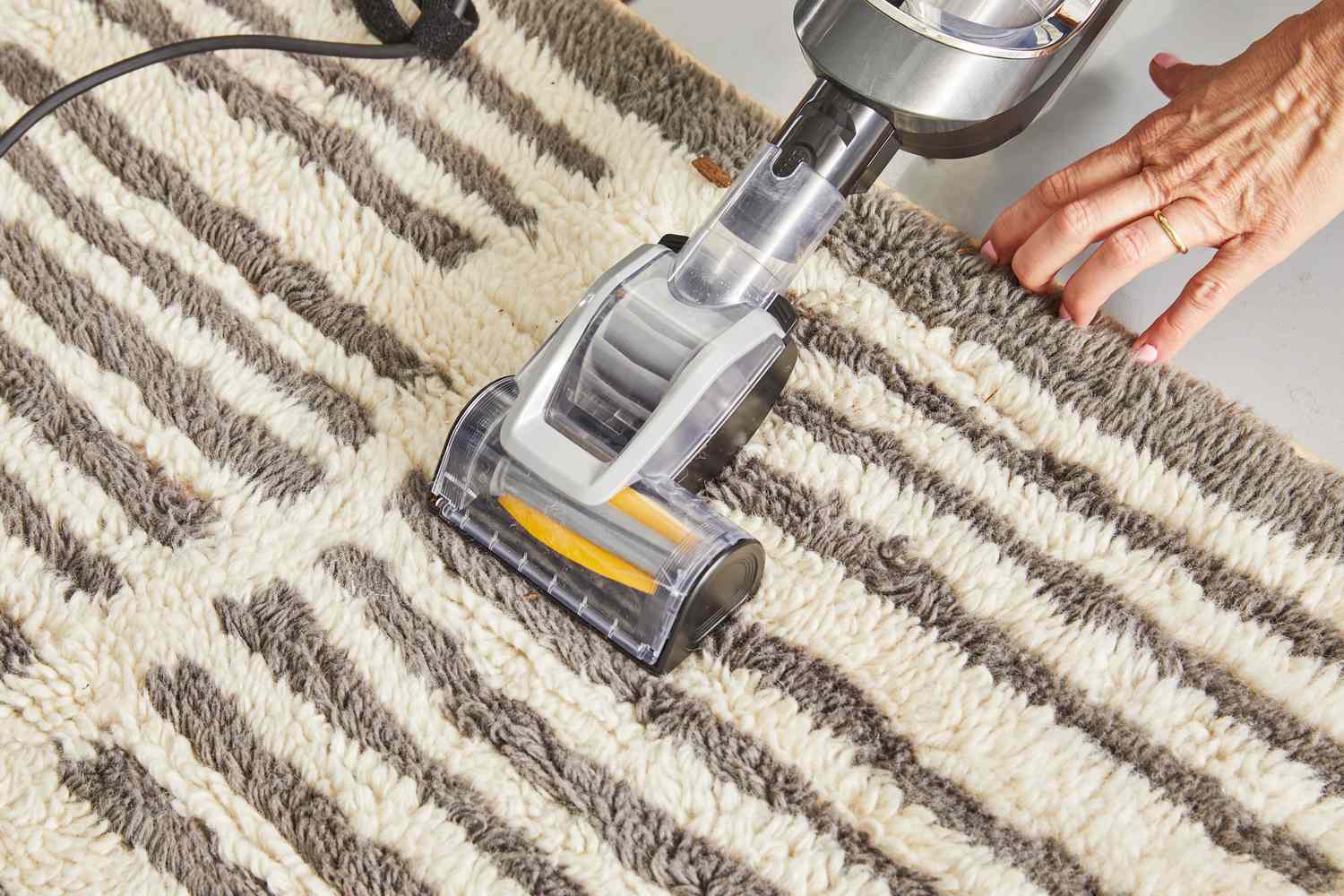 A person vacuuming the AllModern Machine Washable Hand-Woven Wool Ivory/Charcoal Area Rug