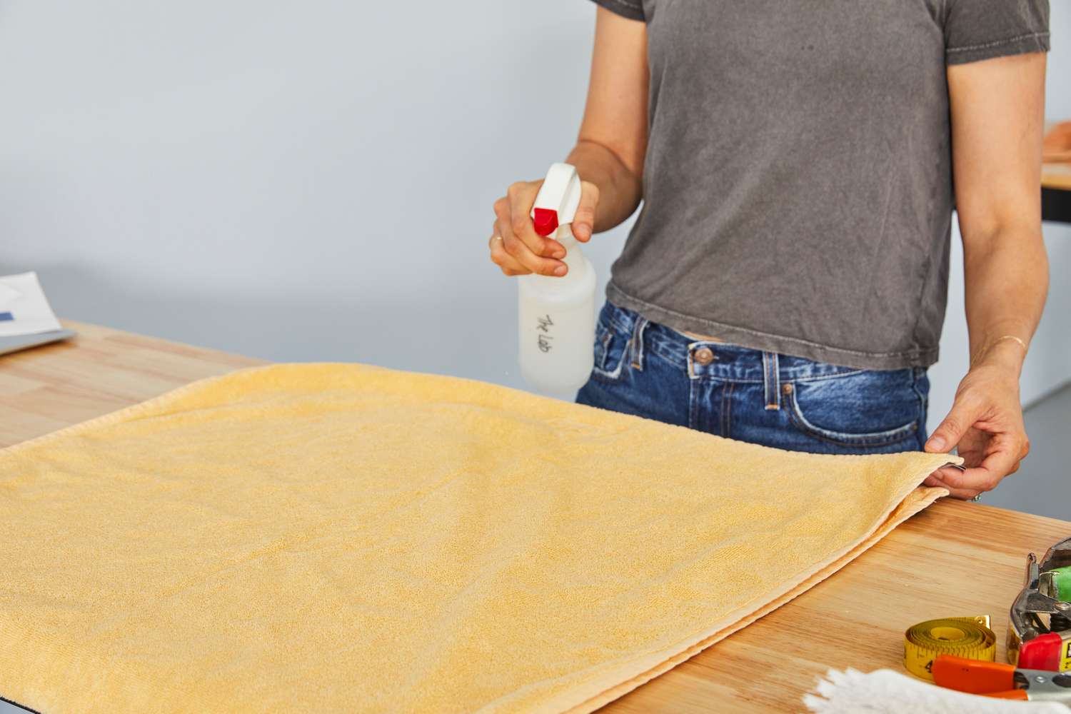 Person using a spray bottle on a Hay Mono Cotton Bath Towel on a wooden table 