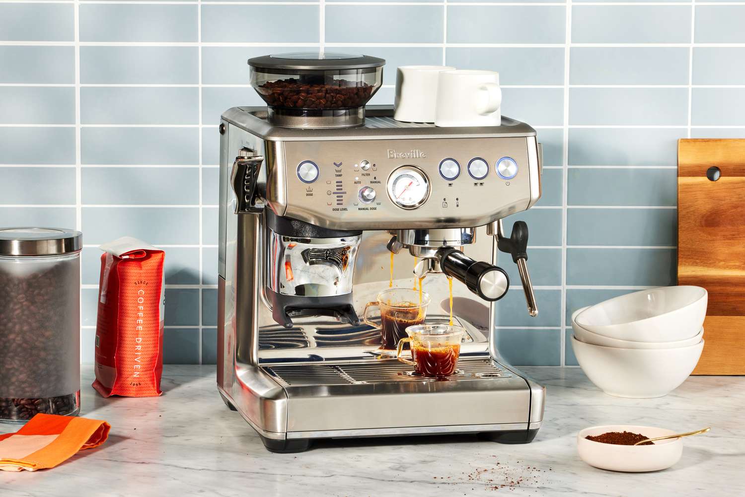 The Breville Barista Express Impress sitting on a counter next to coffee beans.