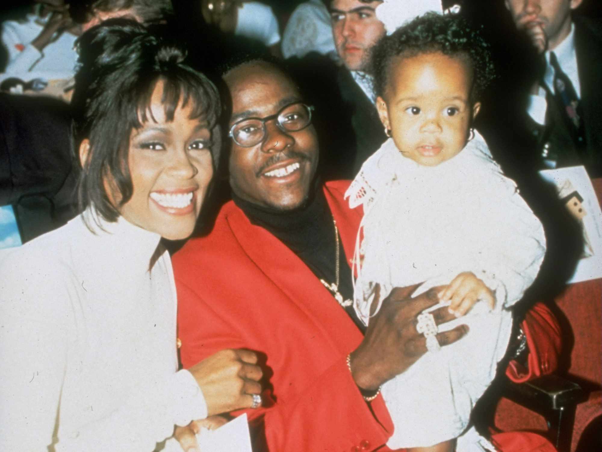 Whitney Houston sitting w. singer husband Bobby Brown, who is holding their infant daughter Bobbi
