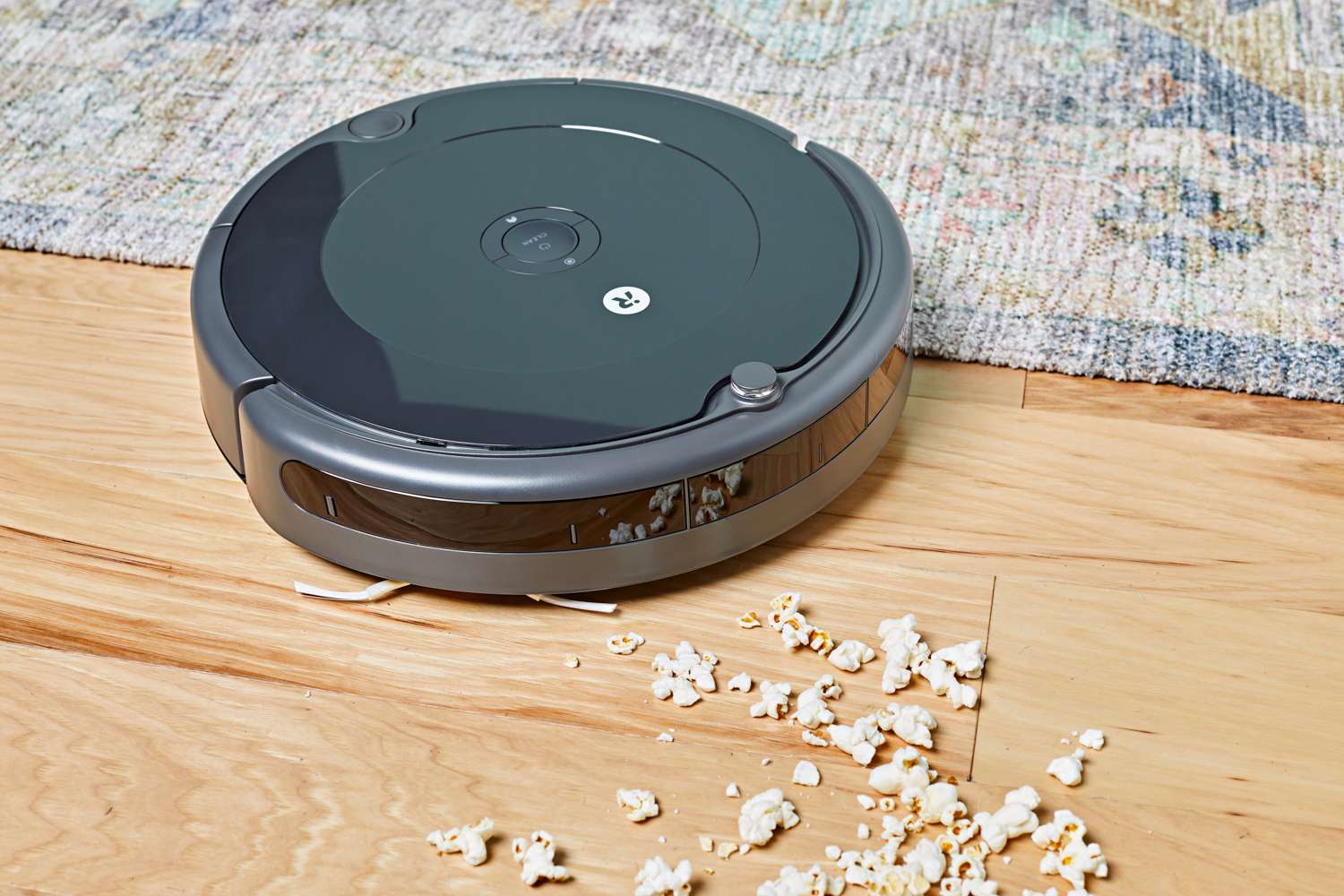 iRobot Roomba 694 Robot Vacuum cleaning popcorn from a hardwood floor near a rug