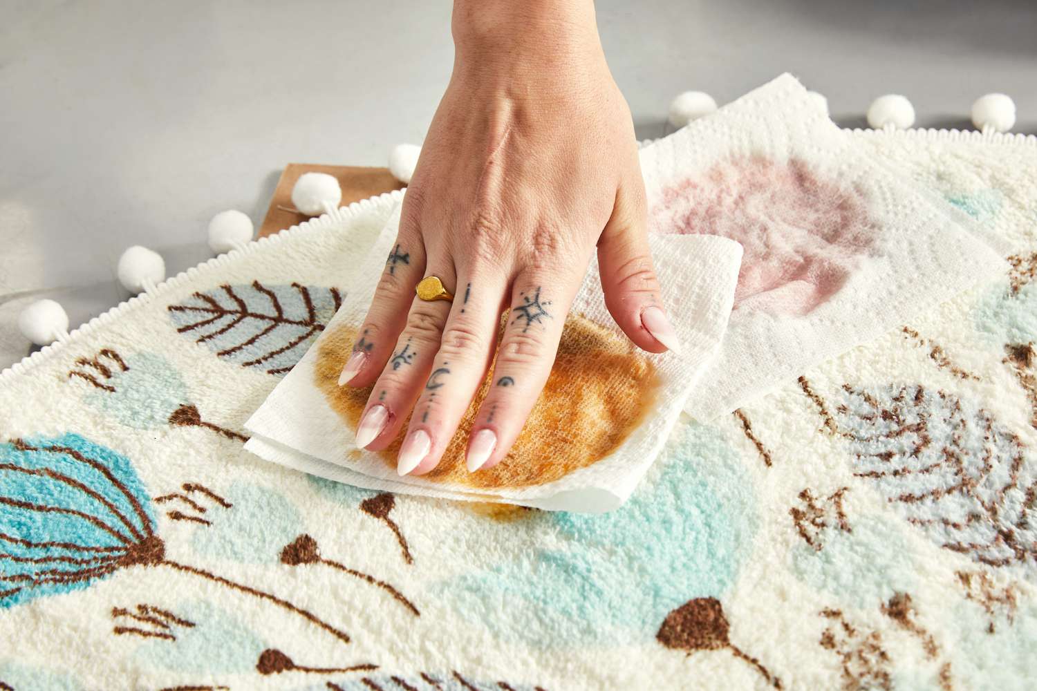 A person cleaning up big stains on the Uphome Pom Pom Round Floral Rug with a paper towel