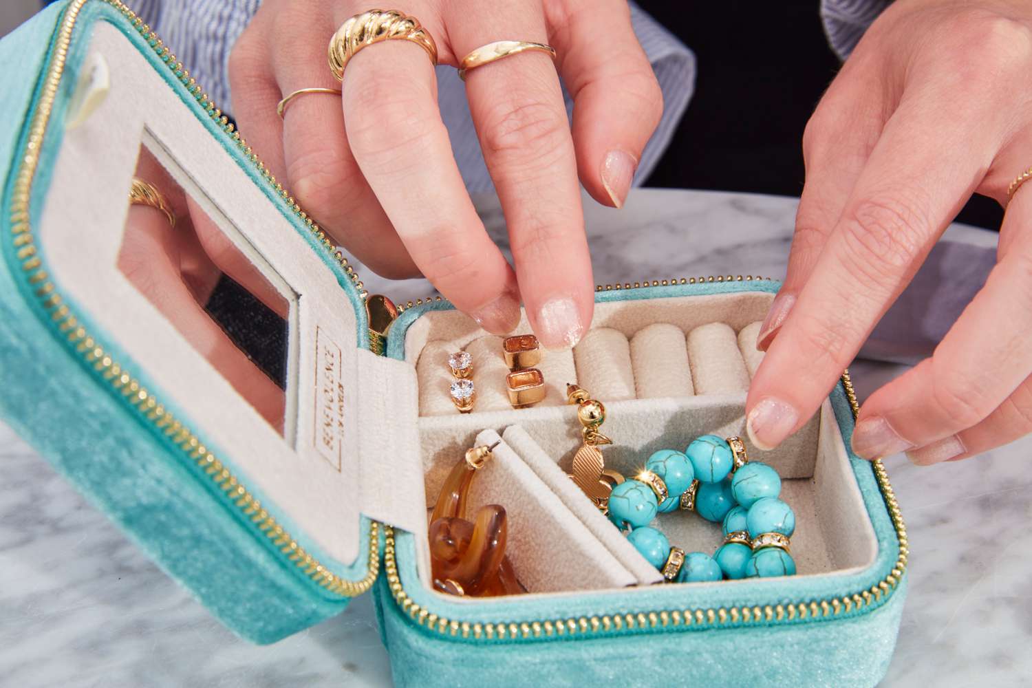 A person places jewelry inside the Benevolence Plush Velvet Travel Jewelry Box Organizer