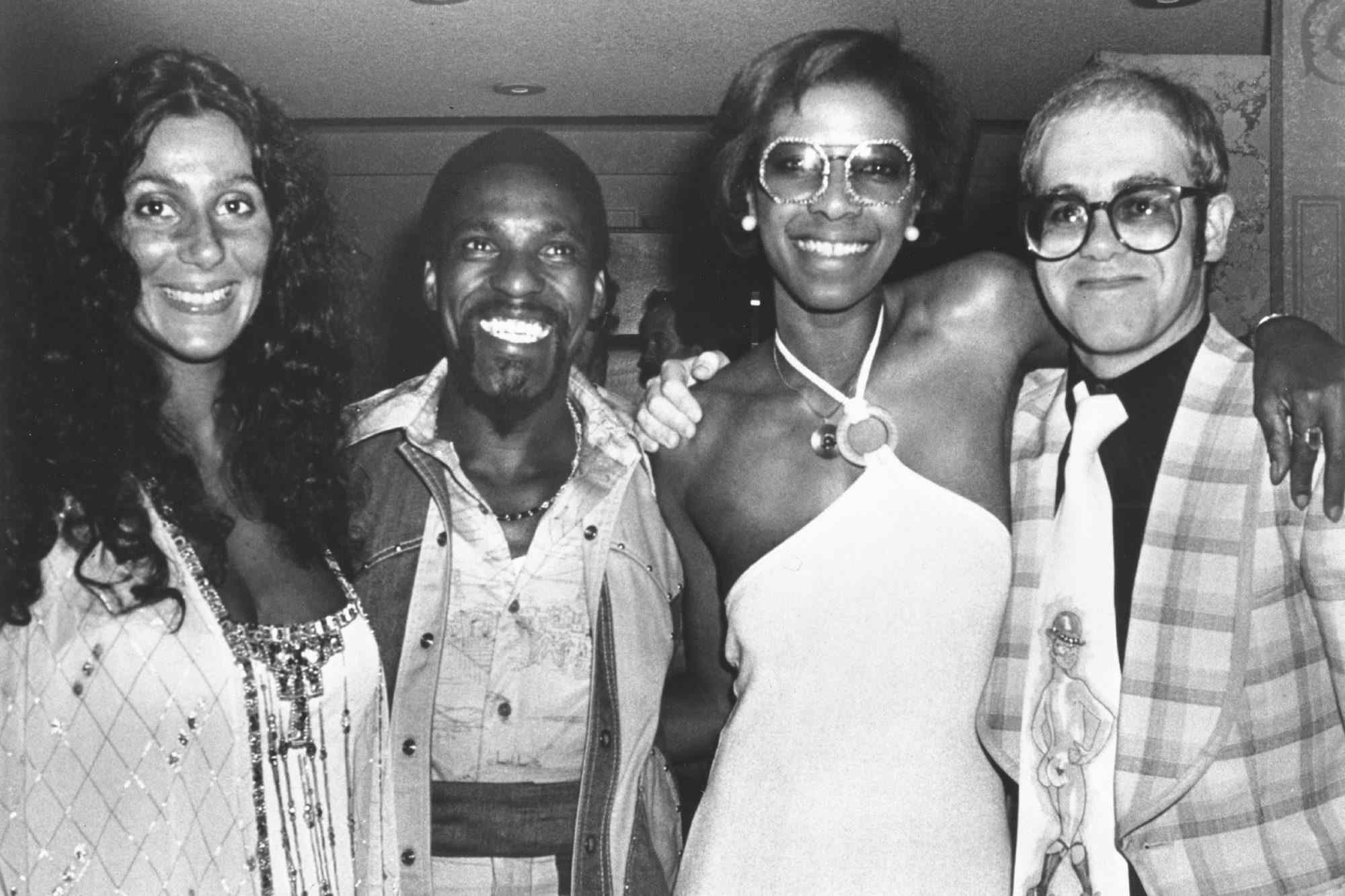Pop singer Elton John poses for a portrait with with fellow popular singers Cher (left), Al Wilson and Natalie Cole at a Wings concert at the Forum in June 1976 in Inglewood, CA