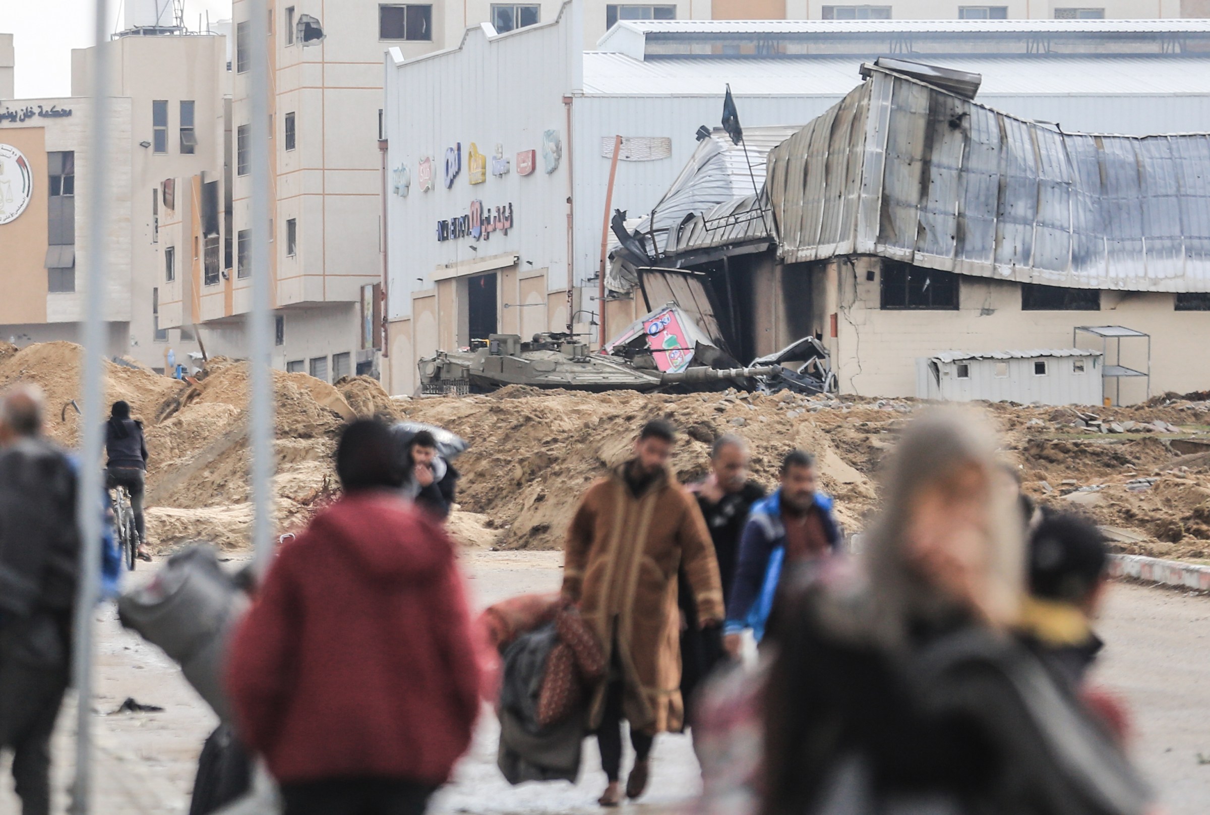 An Israeli tank is seen as Palestinians leave the area of Nasser Hospital on January 29, 2024.