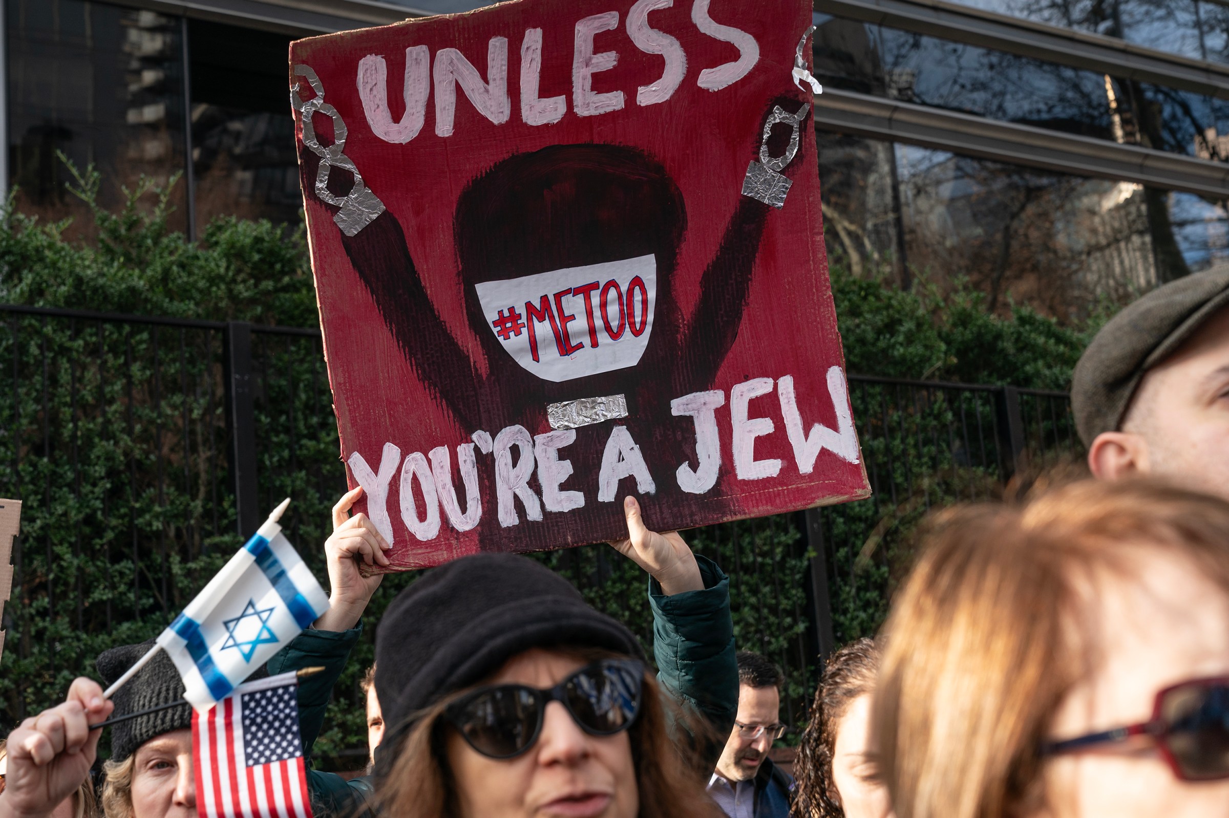 An activist in a swarm of people holds a sign that says “#MeToo unless you’re a Jew.”