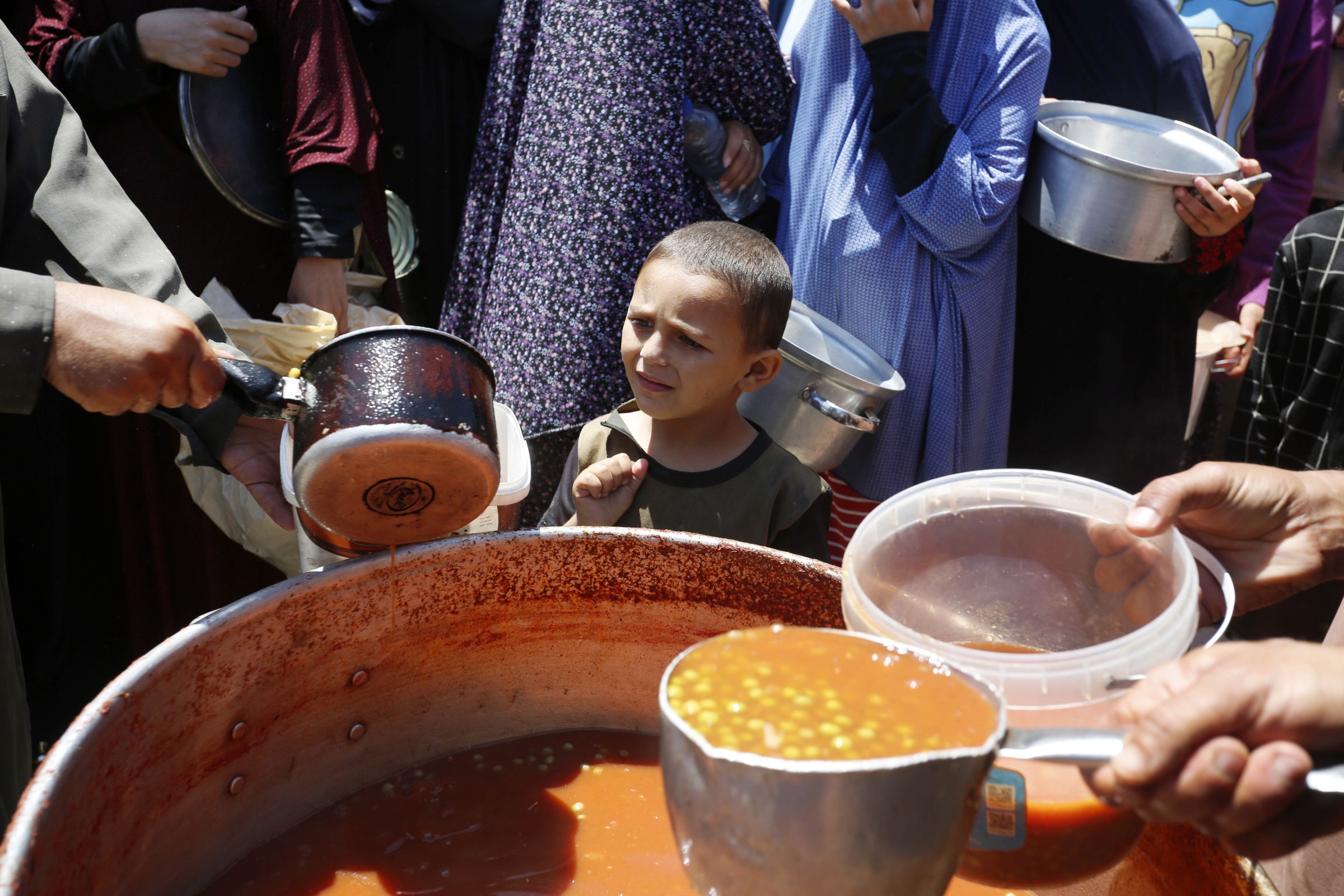 Palestinians displaced from Rafah due to Israeli attacks wait in long queues to get a bowl of food distributed by charity organizations in Deir al-Balah, Gaza, on May 13, 2024. 