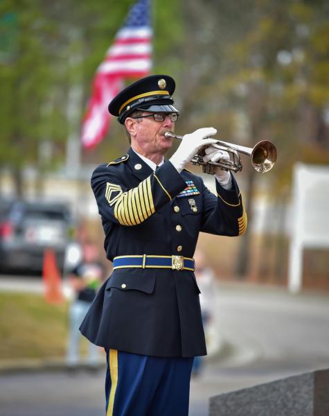 a white soldier playing the trumpet in dress blues and white gloves in front of the american flag