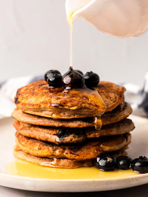 Drizzling a stack of the vegan blueberry pancakes with maple syrup.