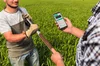 Two people holding a long device for taking a soil moisture sample, one person is holding a phone with an app open