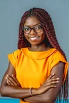 Oiza, with her arms crossed and wearing black glasses and an orange top, smiles at the camera for a headshot image.