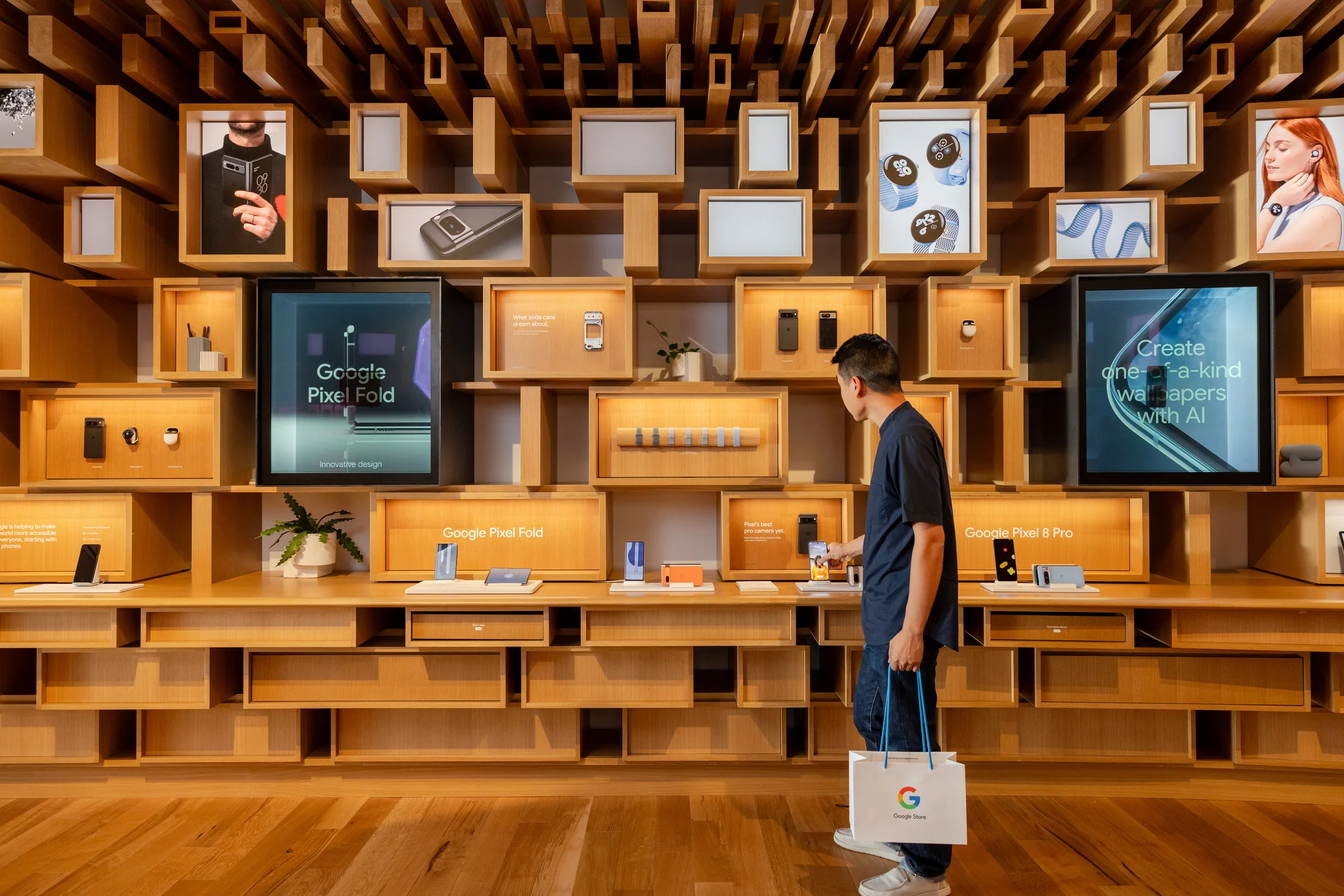 A photo of the interior of the Google Store with a man looking at the Google hardware that's displayed, and he is holding a shopping bag with a Google "G" on it.