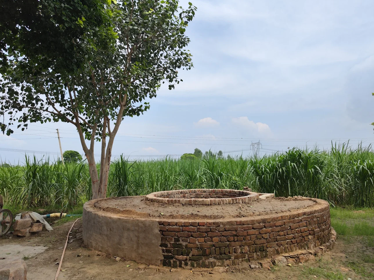 A water well in front of a tree and a field.