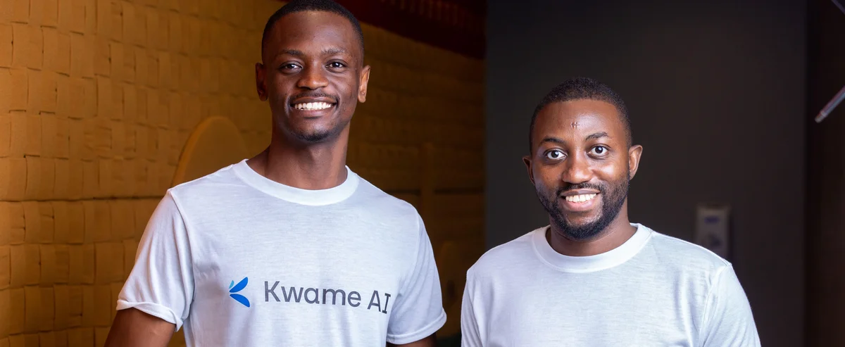 Two men wearing white t-shirts reading "Kwame AI" face the camera and smile.