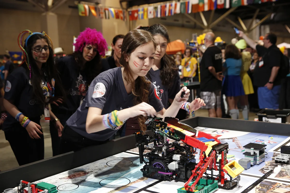 Young woman being cheered on by her teammates while she works on a small robot made of Legos