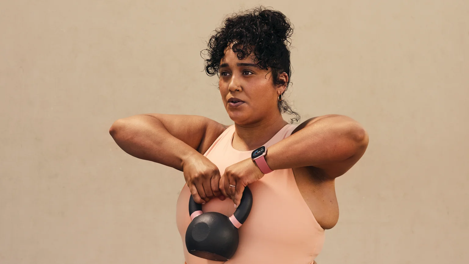 A woman  holding a kettlebell with Versa 4 on her wrist.