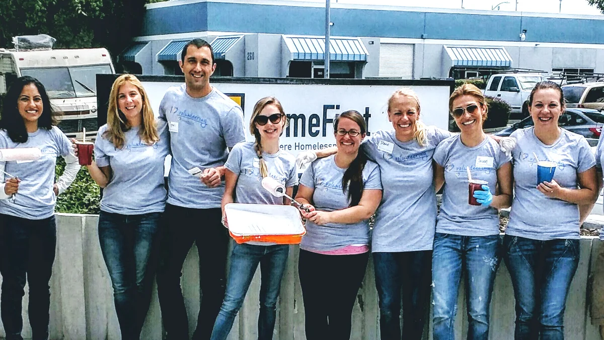 Megan and seven other Googlers stand outside holding paint brushes and cups of paint for a volunteer activity.