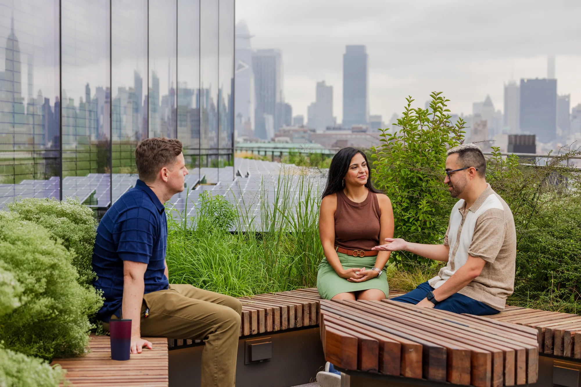 Three Googlers sit outdoors on wood benches, with greenery and solar panels in the background.