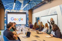 Googlers and clients sit in an executive board room, two women stand at the white board and are overseeing the meeting.
