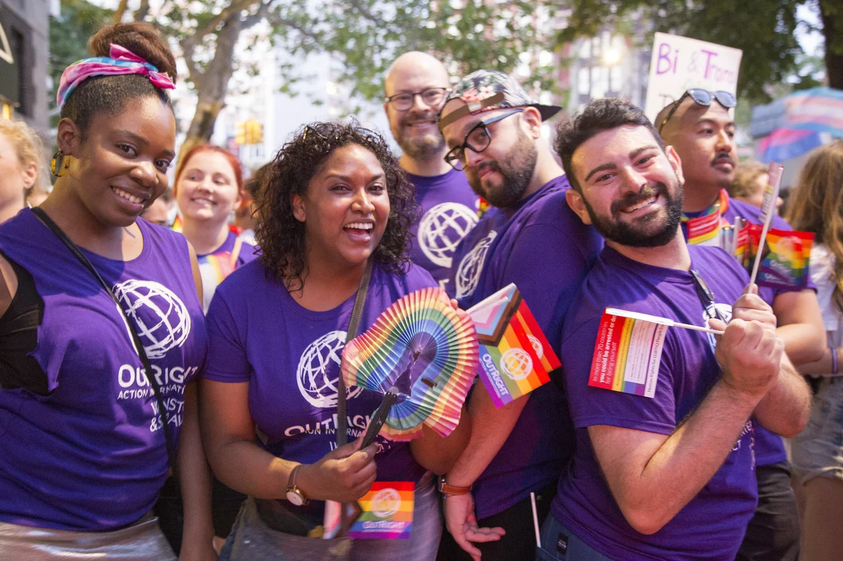 People wearing purple OutRight T-shirts and carrying Pride flag paraphernalia. Photo credit: Hanna Benavides
