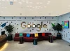 A reception area in Google Dubai’s office with a red couch, three black side tables, and the word Google spelled out in tiles on a wavy-looking wall.