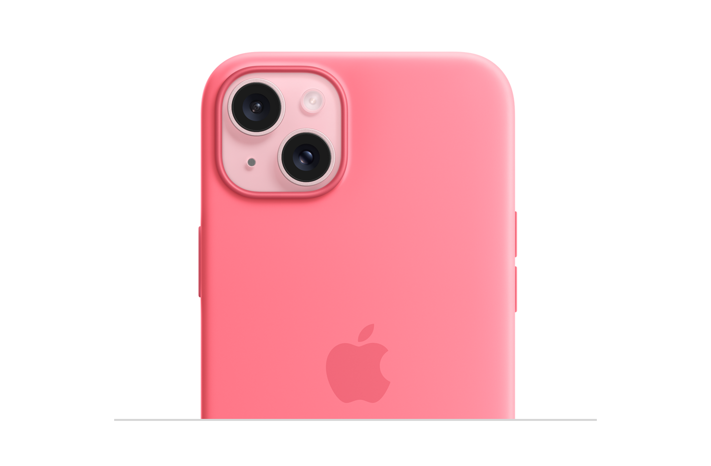 MagSafe-rögzítésű rózsaszín szilikontok, közepén az Apple logóval, rózsaszín iPhone 15-ön, amely a tok kameranyílásán keresztül látszik.