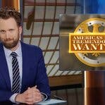 Jordan Klepper sits at a desk on the set of The Daily Show. Next to him is a graphic that says, “America’s Most Tremendously Wanted.”