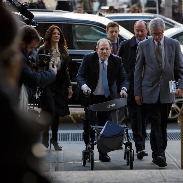 Harvey Weinstein using a walker on the sidewalk, surrounded by lawyers and others.