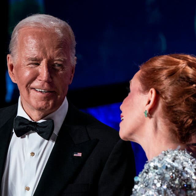 President Biden, in a tuxedo, listening to a woman in an evening gown next to him.
