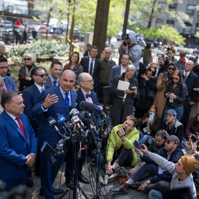Harvey Weinstein’s lawyer, Arthur Aidala, gestures as he speaks in front of microphones. Reporters and photographers are standing around him. 
