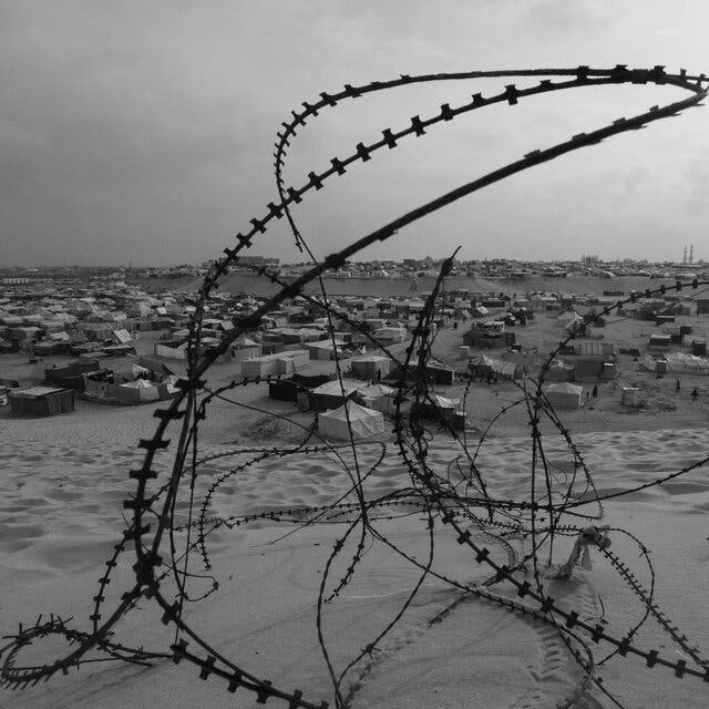 A tangle of barbed wire rests in the sand in front of a camp for displaced Palestinians in Rafah.