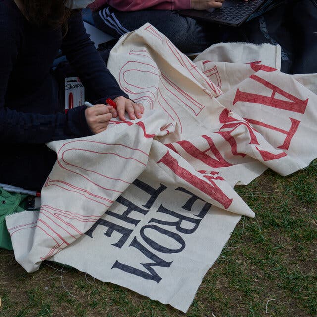 Students at Columbia sitting on grass design a protest banner. 