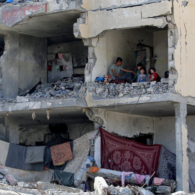 Children stand in a room in a bombed-out building. In other rooms, sheets and garments hang from clothes lines.
