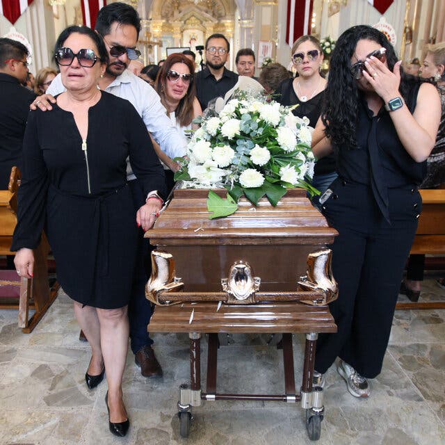 People surround a coffin with a flower arrangement on top.
